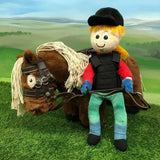 Plush toy with blonde hair wearing a ponies body protector red shirt and blue gloves seated by a brown plush horse
