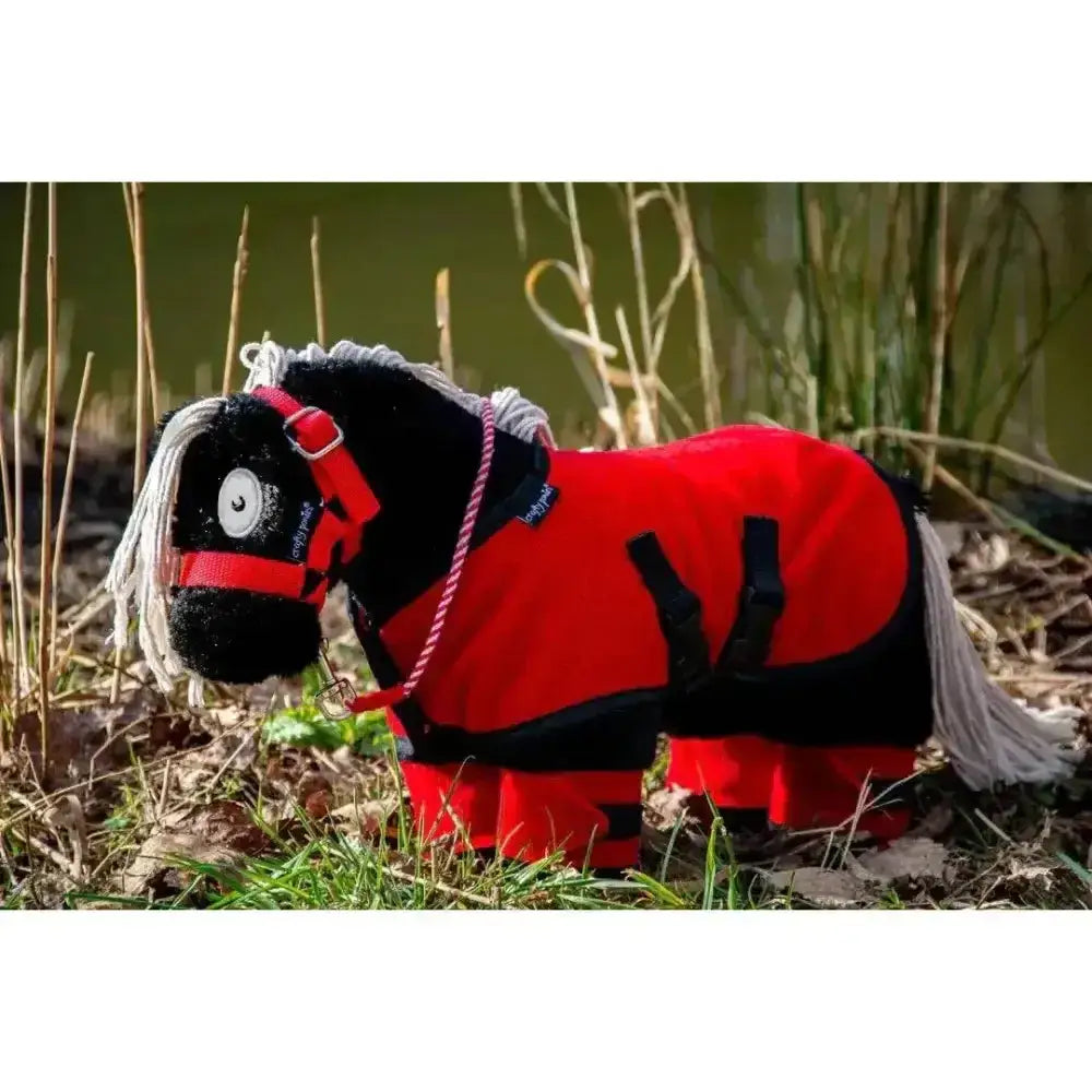 A plush black pony with white mane and tail wearing a red and black riding coat in the crafty ponies fleece rug set