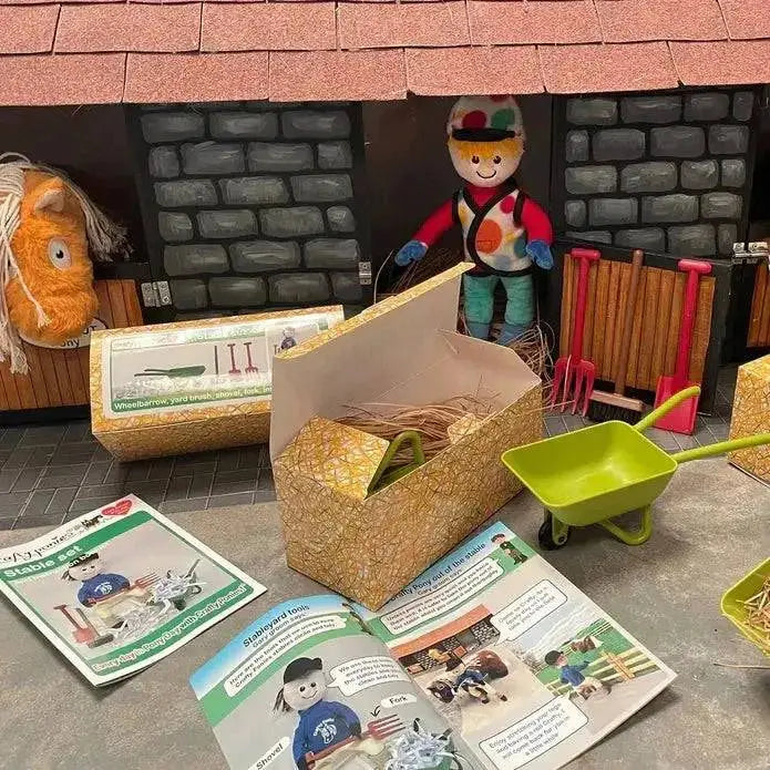 A green plastic toy wheelbarrow with black wheels and handle from crafty ponies muck out set with stable fork and yard brush