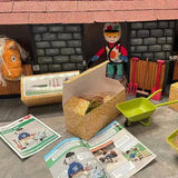 A green plastic toy wheelbarrow with black wheels and handle from crafty ponies muck out set with stable fork and yard brush