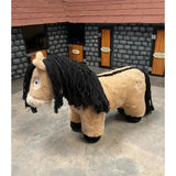 A plush tan soft toy pony exmoor with black yarn mane and tail from crafty ponies standing by a miniature stable