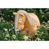 A crafty ponies soft toy pony palomino with plush light golden fur and frayed beige mane sitting in grass and snowdrops