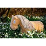 A plush crafty ponies toy pony palomino with a light tan body and white mane stands in grass with snowdrops