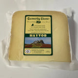 A block of pale yellow curworthy cheese haytor wrapped in clear plastic with a green and cream label showing haytor rock formation