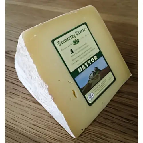 A wedge of pale yellow firm curworthy cheese haytor with a white rind and green haytor brand sticker