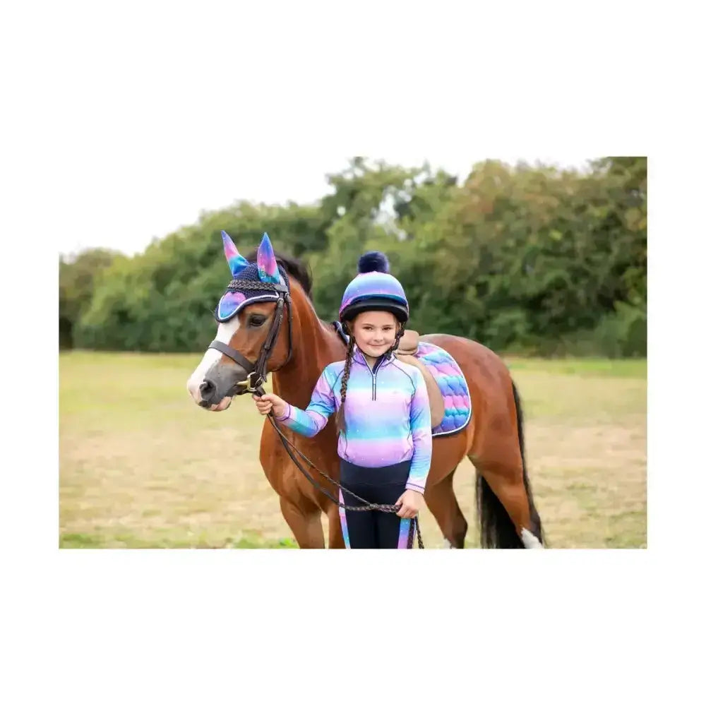 A young girl stands beside a brown horse wearing a dazzling night fly veil with a rainbow saddle pad