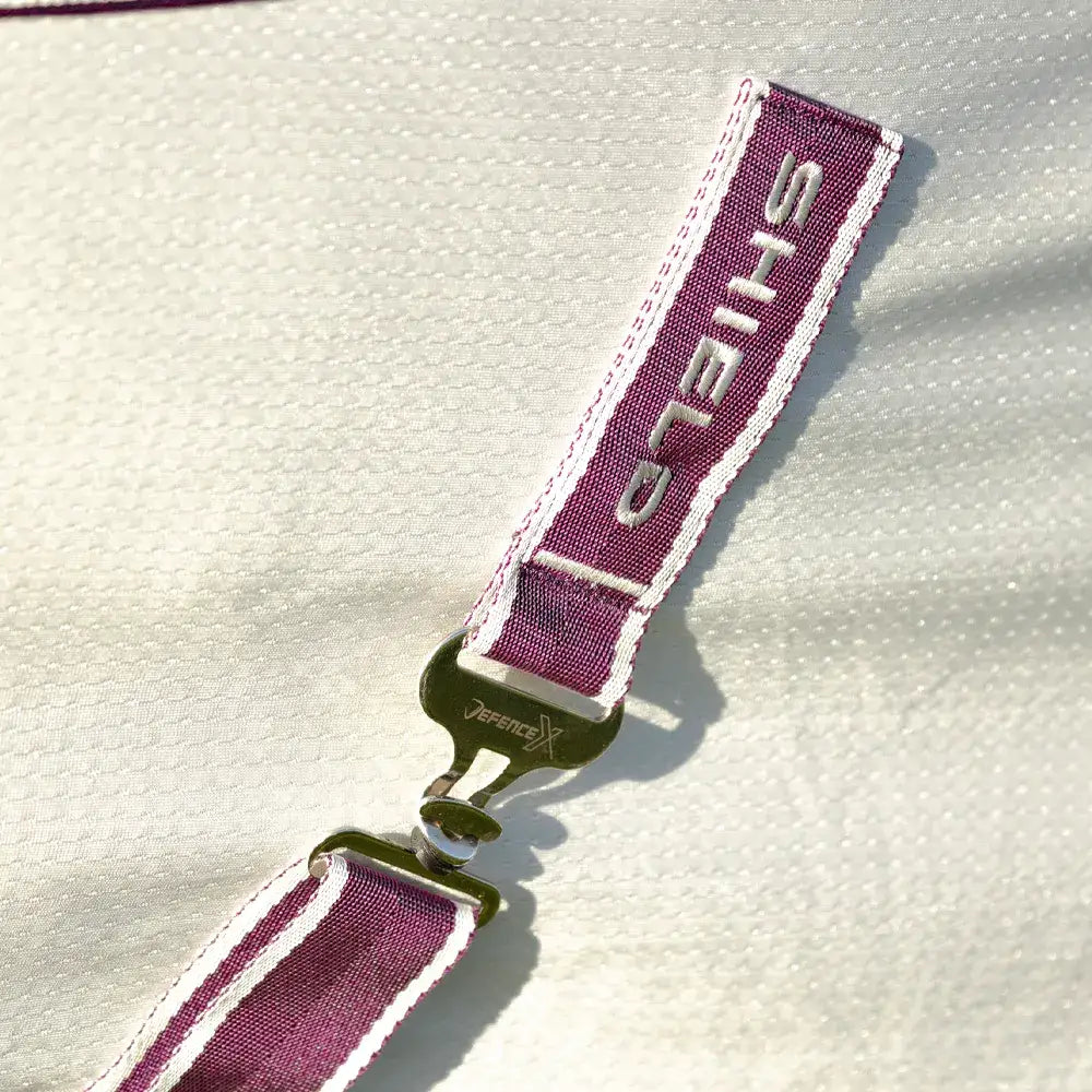 Maroon and white striped fabric strap with silver shield embroidery and metallic buckle on defencex shield sport air cooler rug