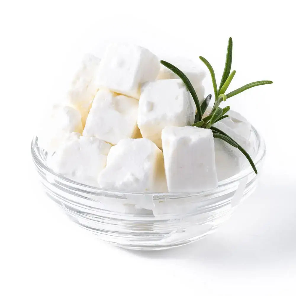 A clear glass bowl with cubed white delphi plain greek feta cheese garnished with a fresh green rosemary sprig