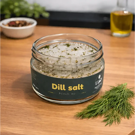 A clear glass jar of white crystalline dill herb infused salt topped with fresh dill by broomhill farm co