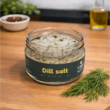 A clear glass jar of white crystalline dill herb infused salt topped with fresh dill by broomhill farm co