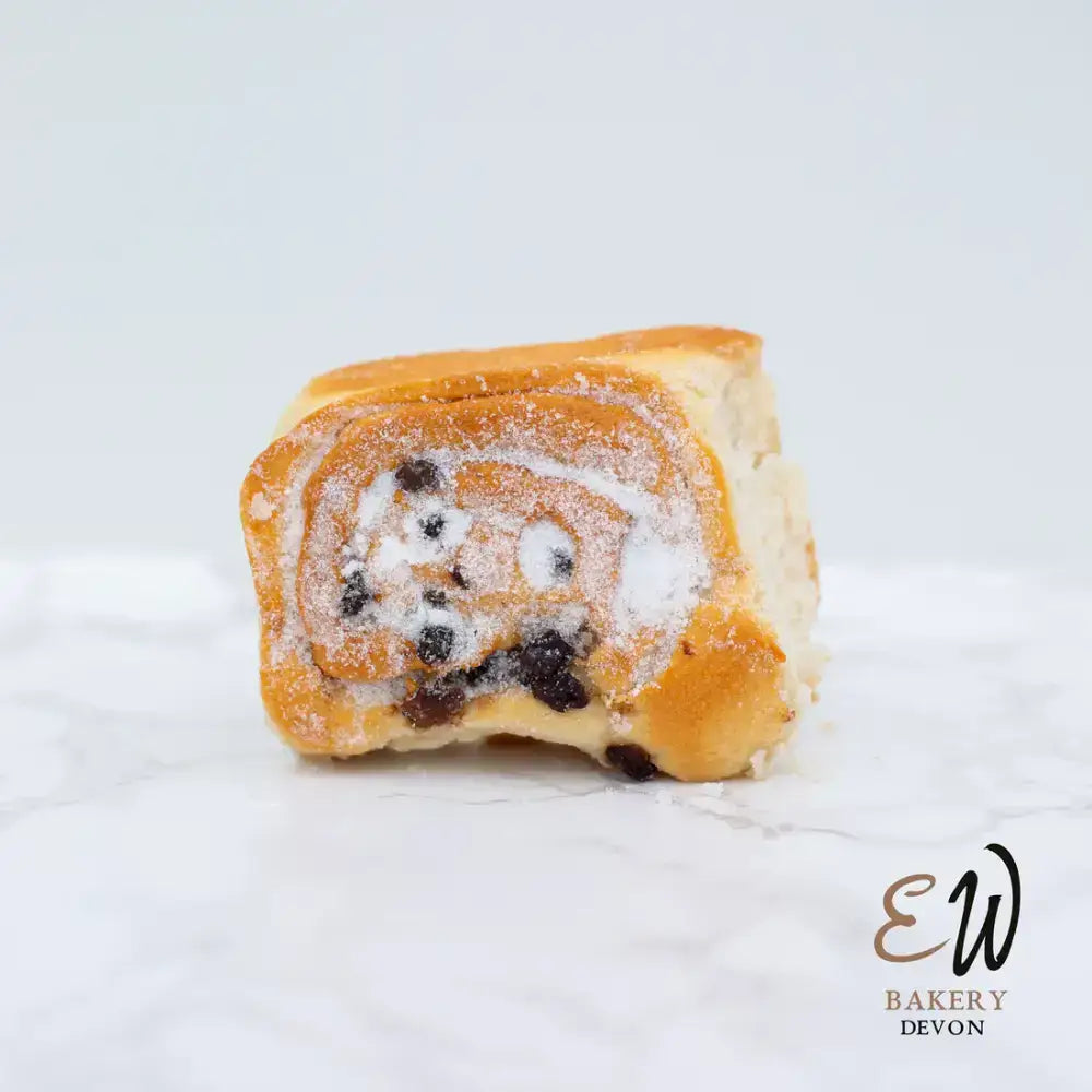 Golden brown west chelsea bun with raisin swirl and powdered sugar dusting in a round white bread style