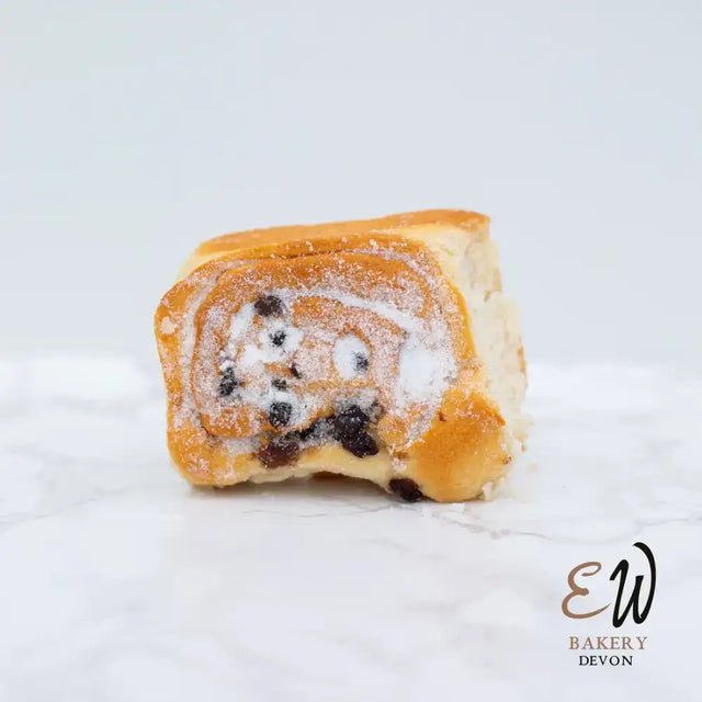 Golden brown west chelsea bun with raisin swirl and powdered sugar dusting in a round white bread style