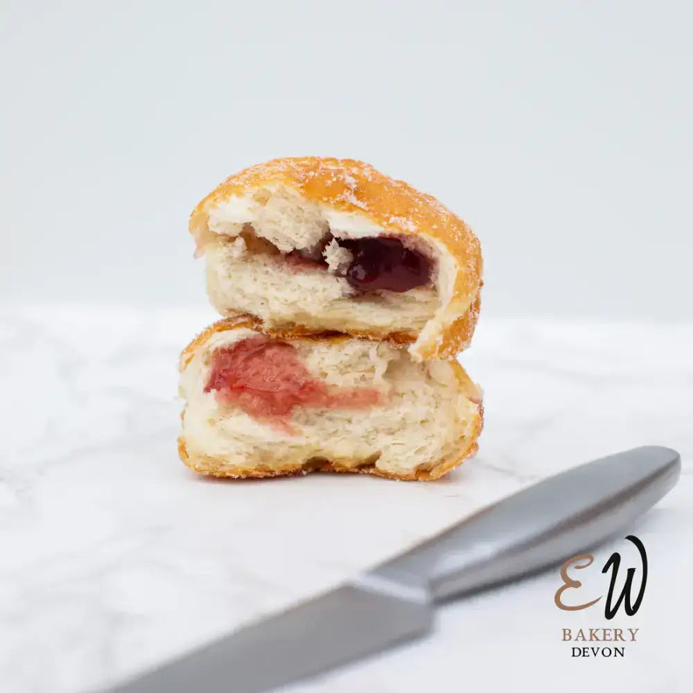 Golden sugar-dusted east & west doughnuts jelly-filled round white bread halves stacked on marble surface