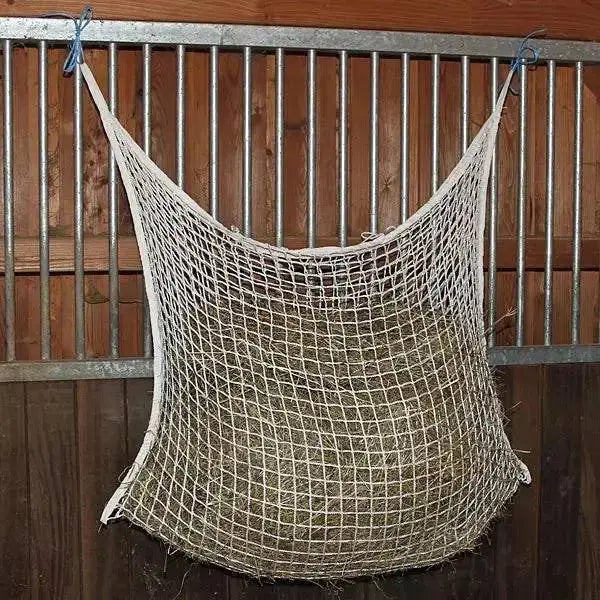 A beige woven dry grass haynet hanging from a metal gate shows the elico brelade continental haynet helps feed horses easily