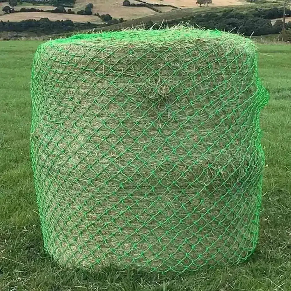 A cylindrical bale of hay wrapped in bright green mesh netting field haynet designed for wild boar field use