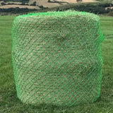 A cylindrical bale of hay wrapped in bright green mesh netting field haynet designed for wild boar field use