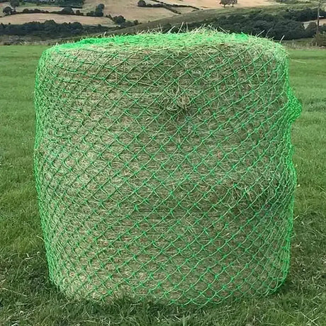 A cylindrical bale of hay wrapped in bright green mesh netting field haynet designed for wild boar field use