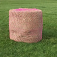 Eliсo wild boar field haynet featuring a pink mesh net wrapping a cylindrical hay bale on green grass