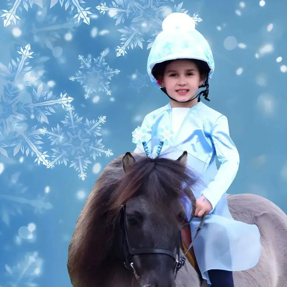A young child wearing a light blue equetech childs fjord snowflake hat silk with a white pom-pom on top