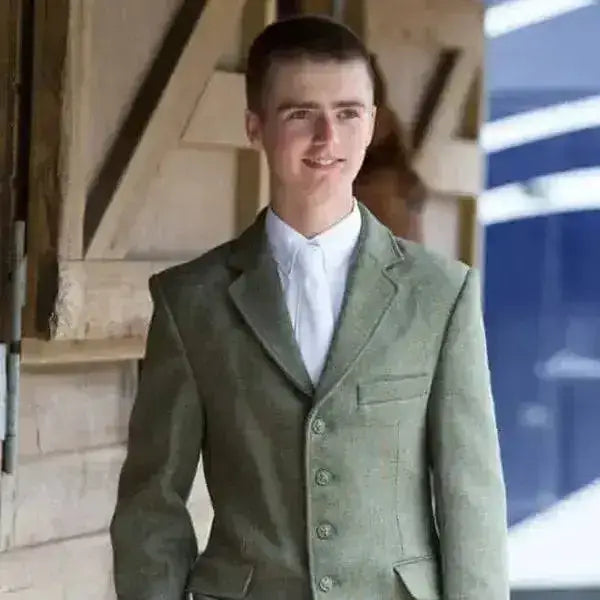 A young man wearing an equetech claydon tweed boys riding jacket in olive green tweed with matching buttons and white shirt