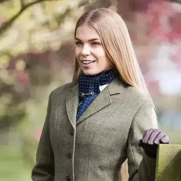 A woman wearing an equetech claydon tweed riding jacket in green herringbone tweed with a dark blue polka-dot scarf