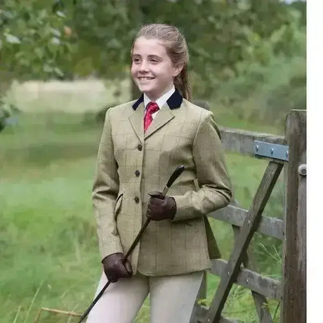 A young girl wears an equetech junior foxbury deluxe tweed riding jacket in beige with black collar trim and brown gloves