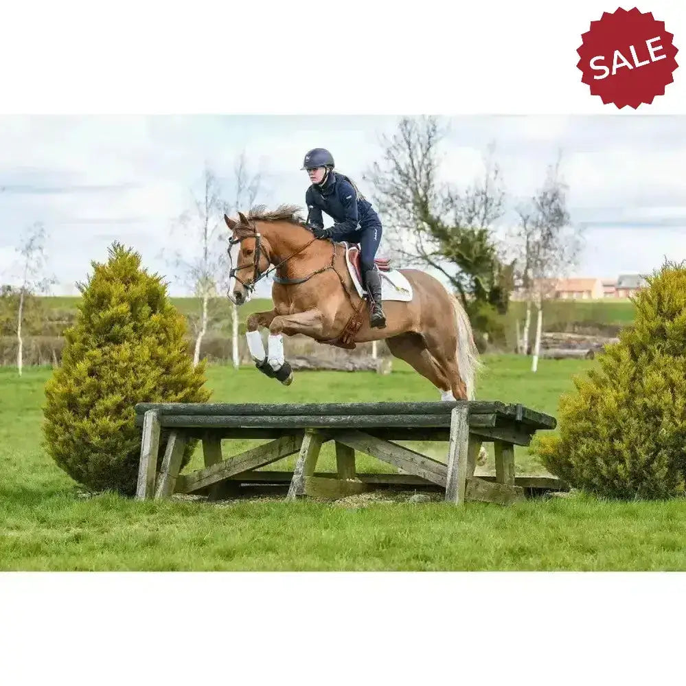 A chestnut horse mid-jump wearing white equilibrium tri-zone impact sports boots for cross country protection