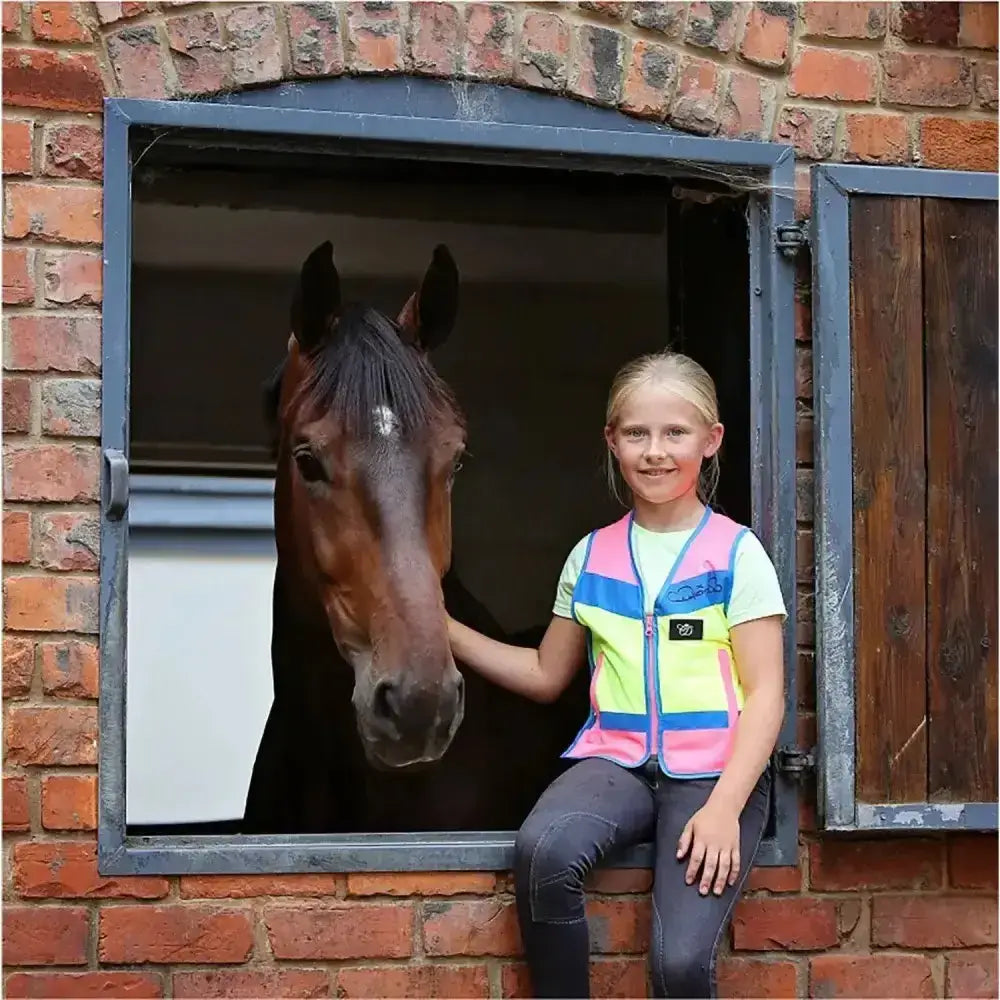 The girl wears equisafety childrens hi-vis multi coloured waistcoat with pink yellow and blue reflective stripes