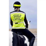 Rider wearing bright yellow equisafety hi-vis waistcoat with reflective stripes and black horse in training text on back