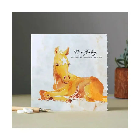 A fanciful dolomite card featuring a golden foal with white markings on textured paper for new baby greetings
