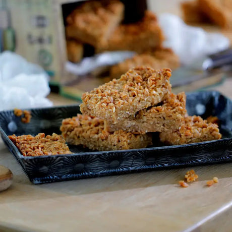Golden-brown flapjack handmade cake oat bars with crunchy texture stacked on ornate black ceramic tray