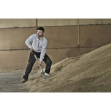 A man wears a fort tattersall shirt green brushed flannel shirt holding a shovel next to a large grain mound