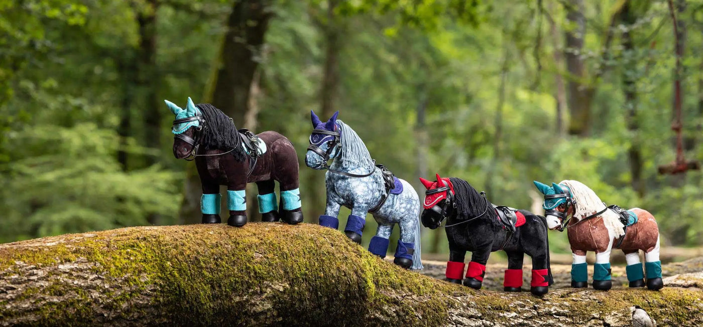 Four whimsical, stylized toy horses with colorful accents and unique markings stand in a row on a mossy log.