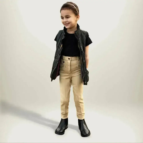 A child wearing gallop childrens classic beige plain jodhpurs paired with black leather vest and boots