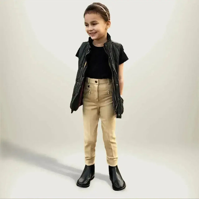 A child wearing gallop childrens classic beige plain jodhpurs paired with black leather vest and boots
