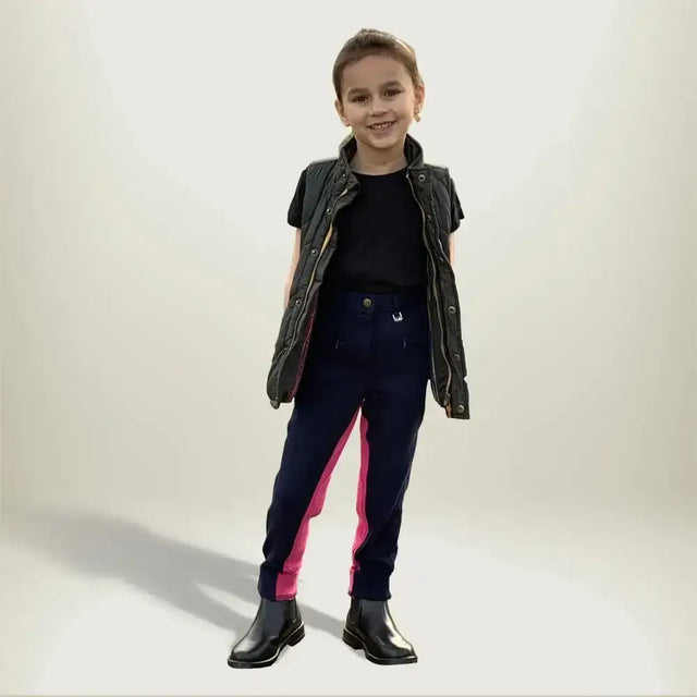 A child wearing gallop children’s two tone jodhpurs with eye catching contrast pink side panels and shiny black boots