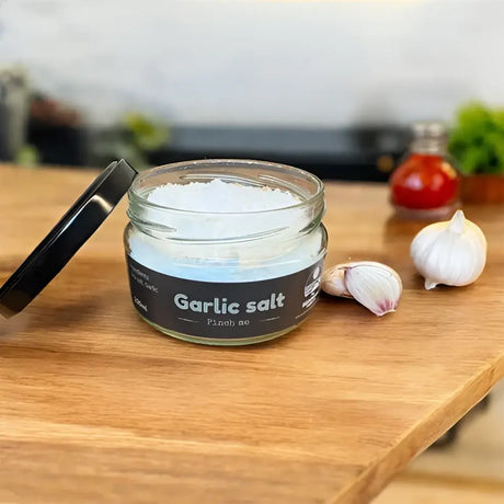 Clear glass jar with black lid containing white garlic herb infused salt by broomhill farm co