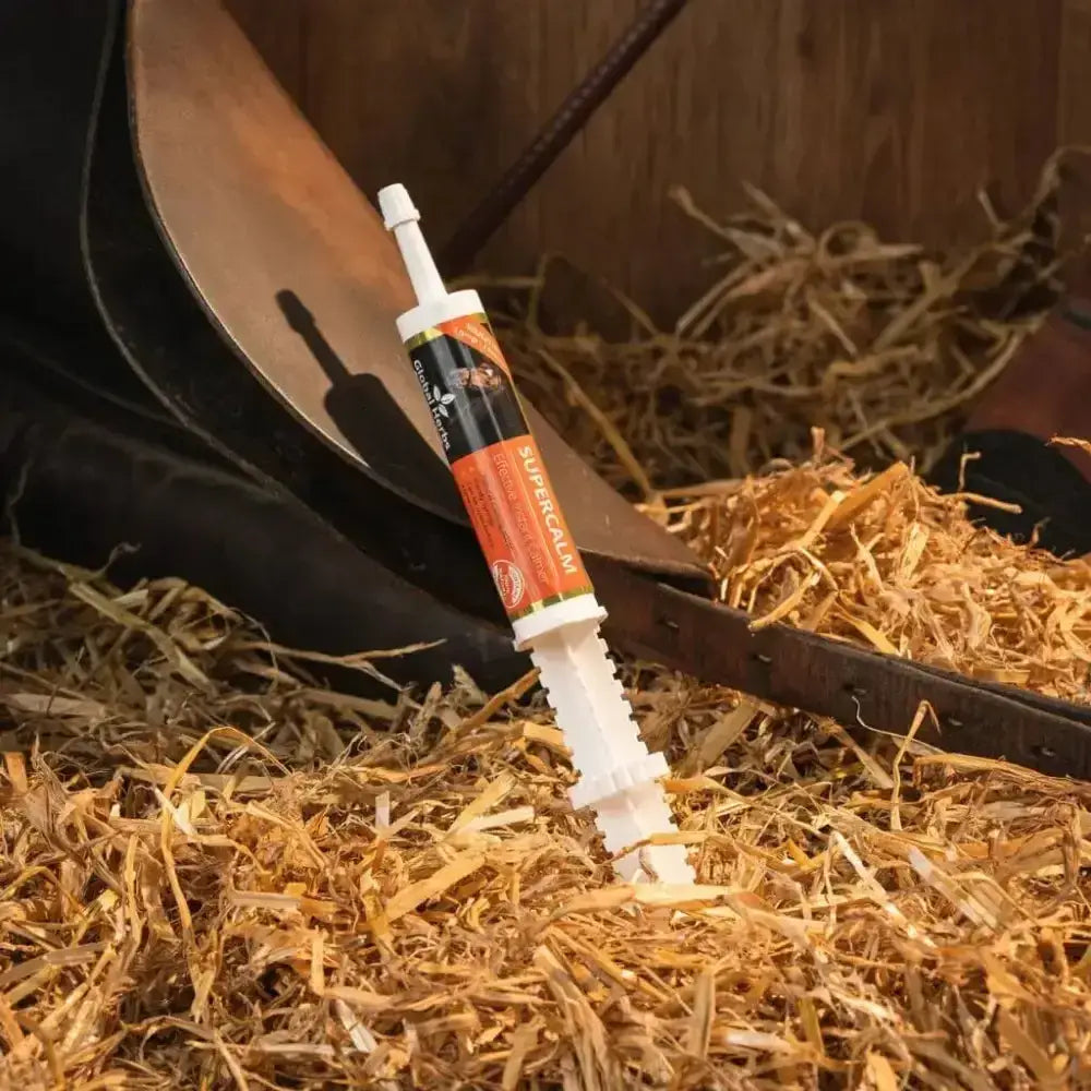White plastic syringe with orange and black label reading supracalm resting on straw for global herbs supercalm instant syringe calming herbal mix