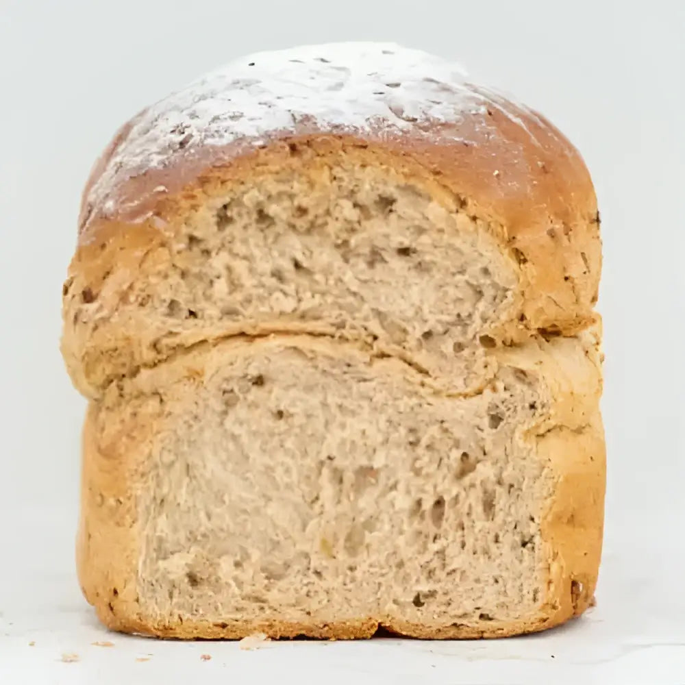 A golden-brown round granary farmhouse loaf with a flour dusting and a soft airy seeded interior