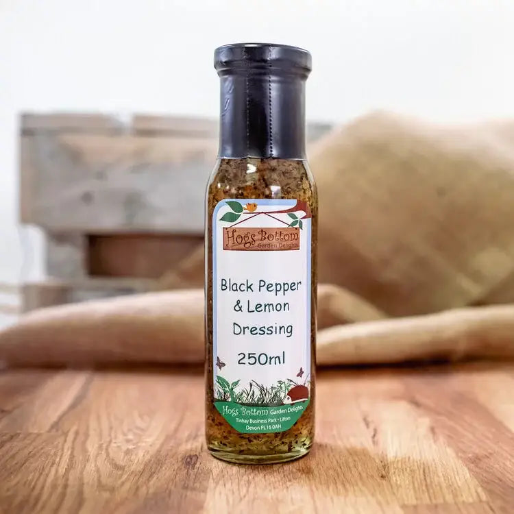 A clear glass bottle with black cap containing hogs bottom black pepper and lemon dressing 250ml