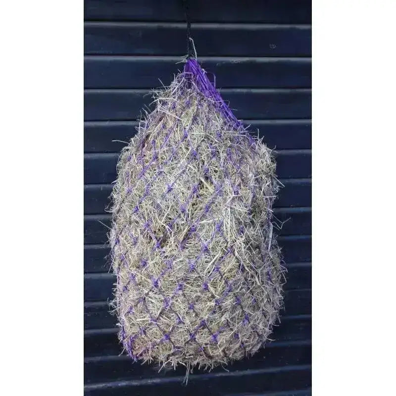 Purple mesh hungry horace greedy feeder haynet filled with dry straw hanging against dark background