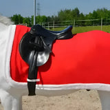 Red saddle blanket with white trim and synthetic white fur under a black horse saddle on hy equestrian christmas santa sheet