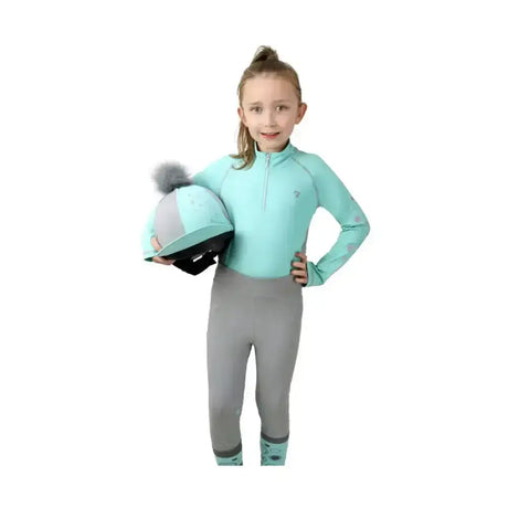 Mint green and gray equestrian helmet with a fluffy pom-pom paired with dynamizs ecliptic riding tights for riding fun