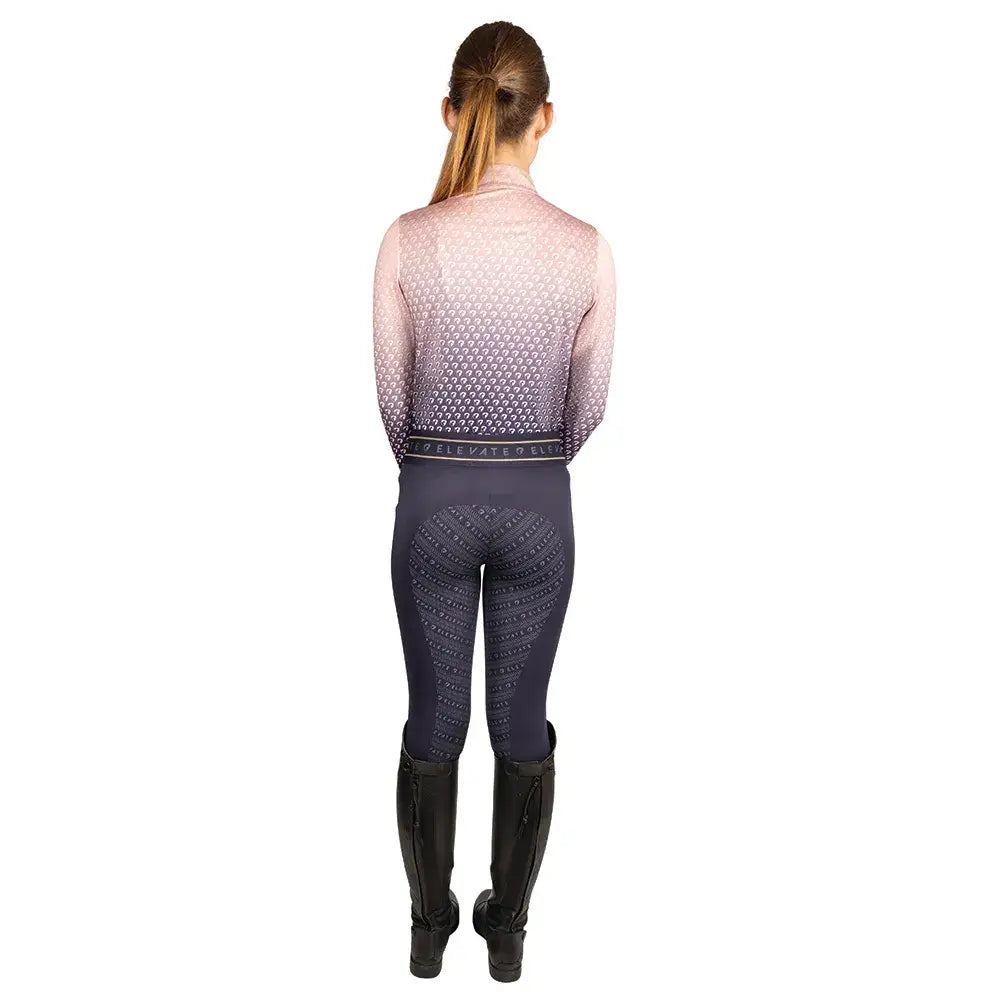 A woman wearing hy equestrian elevate allure mizs ombre base layer in gradient pink to purple with dark gray grip riding pants