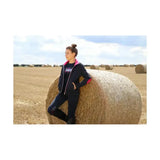 A young woman leans on a hay bale wearing black and pink mizs eugenie breeches with silicone knee patches and bi-stretch material