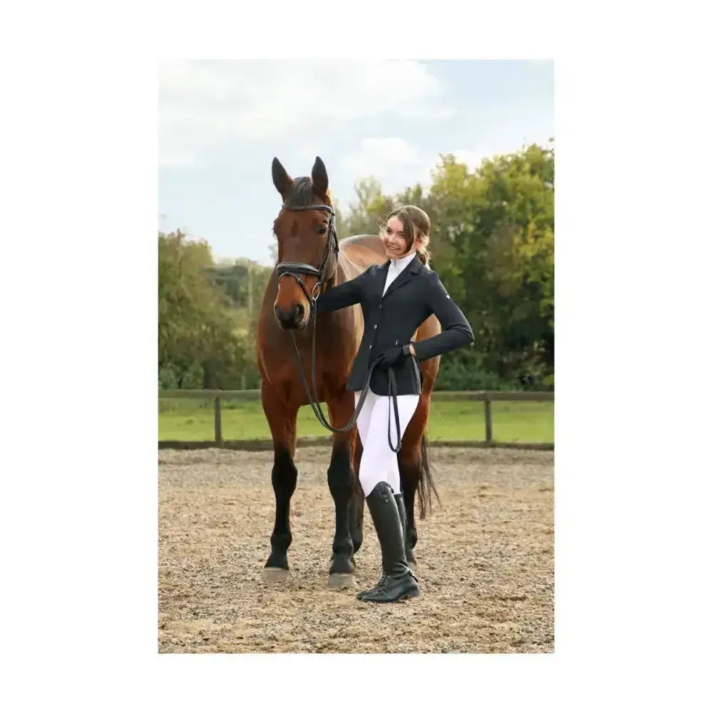 A woman in hy equestrian silvia jacket ladies made of technical material stands beside a brown horse with black bridle