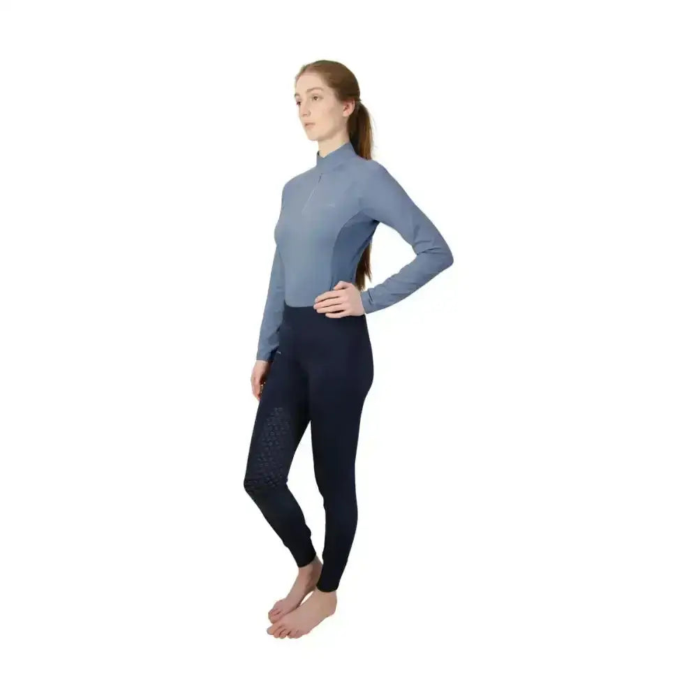 A woman wearing a light blue hy equestrian synergy base long sleeve top and navy synergy base layer leggings