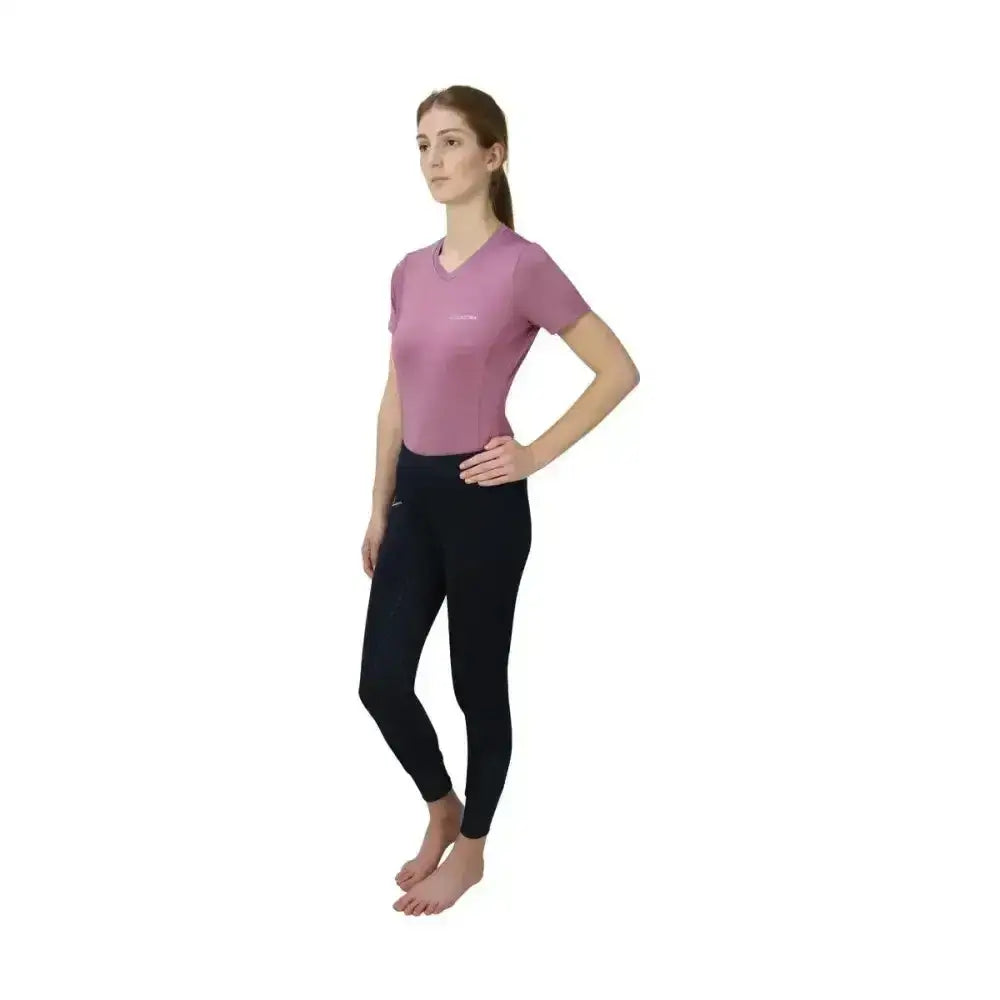 A woman wearing black Hy Equestrian synergy riding tights that allow unrestricted movement and a soft lavender top