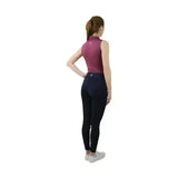 A woman wearing a sleeveless magenta hy equestrian synergy sleeveless polo with black leggings showing sleeveless polo features