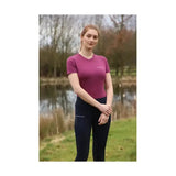 A woman wearing a magenta hy equestrian synergy t-shirt fig with a small logo and dark navy leggings with side zipper pocket